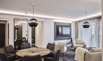 A modern living room with a round dining table and comfortable armchairs. Large windows let in plenty of daylight, and the atmosphere is cozy and inviting.