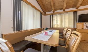 A bright room with a large table and comfortable seating. The walls are paneled with wood and there are large windows with blinds.
