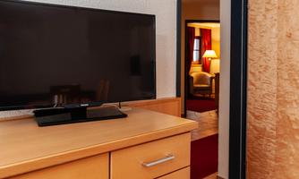 A television is placed on a wooden dresser in a bright room. In the background, a cozy seating area is visible.