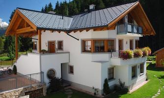 A modern house with a beautiful garden and blooming plants. The architecture combines wood and white and is surrounded by trees.