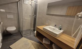 A modern bathroom with a shower cabin and a minimalist washbasin. The walls are in neutral gray tones, and there is a wooden cabinet.