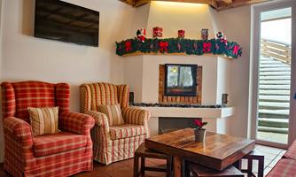 A cozy living space with two checkered armchairs and a fireplace. The room has a warm atmosphere and large windows that lead to an outdoor staircase.