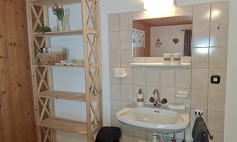 Modern sink and a large mirror additionally in the room. Next to the sink is an open shelf with decoration. The bathroom is located on the floor.