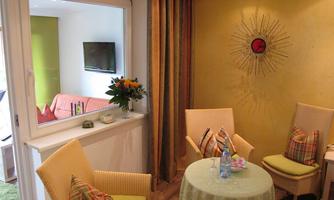 A cozy room with two chairs and a round table. The walls are painted in warm colors, and there is a television in the background.