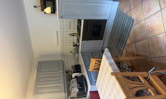 A modern kitchen with gray cabinets and a dining area. The room is bright and friendly with tiled flooring and a large table.
