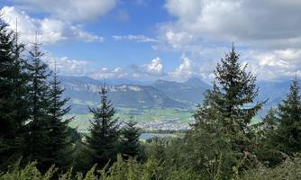 A picturesque mountain landscape with green meadows and a lake in the valley. In the background, there are tall mountains and a blue sky with clouds.