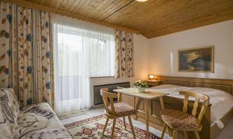 A cozy room with a wooden ceiling, windows with curtains, and a small table. There is a couch and an artistic wall decoration.