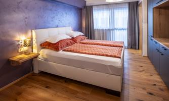 A modern bedroom with a double bed and red bedspreads. The room has wooden floors and large windows that provide plenty of light.