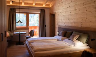 A cozy bedroom with wooden paneling and two single beds. Large windows offer a view outside and let in plenty of daylight.