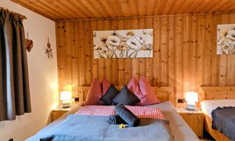 A cozy bedroom with wooden paneling and two beds. Subtle lighting and decorative cushions create an inviting atmosphere.