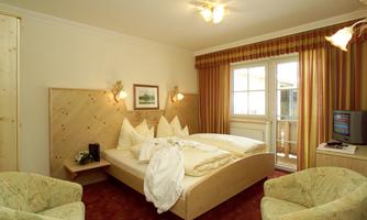A cozy bedroom with a large double bed and two comfortable armchairs. The windows let in a lot of light, and the room features wood-paneled walls.