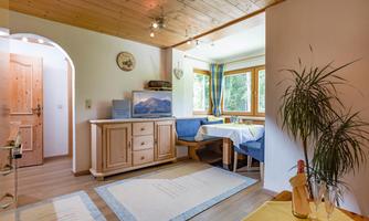 A cozy living space with wooden paneling and large windows. There is a dining table and a dresser, surrounded by blue chairs.