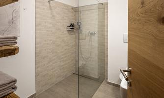 A modern shower with a glass partition and bright tiles. Towels are stored on a wooden shelf.