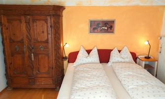 A cozy bedroom with a large wooden wardrobe and two beds. The walls are painted in warm orange, and there is a decorative light next to each bed.