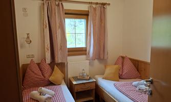 A cozy room with two beds and colorful cushions. The room is bright and has a window overlooking the outdoors.