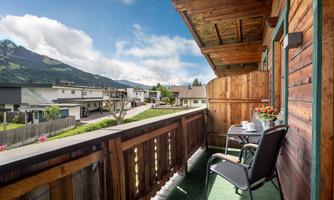 A cozy balcony with a table and chairs, surrounded by a picturesque landscape. In the background, there are mountains and a clear sky.