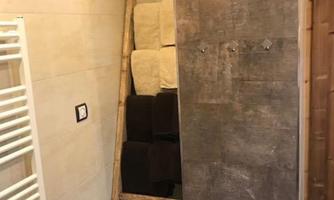 A modern bathroom with a heating coil and a wooden ladder. On the ladder, towels in different colors are stacked.