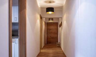A bright hallway with wooden floors and modern lamps. Doors to additional rooms are visible on the sides.