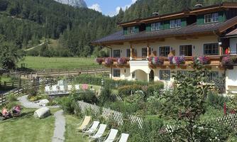 A picturesque building in the mountains with a beautiful garden. Sun loungers and blooming plants surround the terrace.