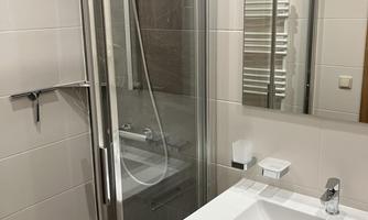 A modern bathroom with a glass shower and a white sink. The walls are brightly tiled, and a large mirror is present.