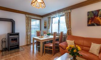 A cozy living room with a dining table, chairs, and a red couch. A fireplace and large windows create a bright, inviting atmosphere.