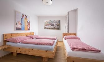 A cozy bedroom with two wooden single beds and checked bedding. Pictures hang on the wall, and the room is designed to be bright and welcoming.