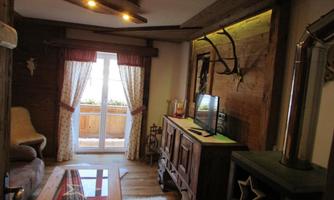 A cozy living space with wooden details and a TV corner. Large windows let in plenty of light and provide a view outside.