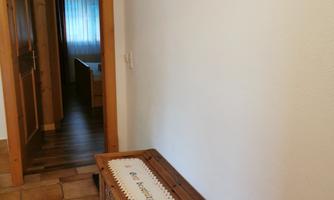 An entrance area with a wooden bench and a tablecloth. A cross hangs on the wall.