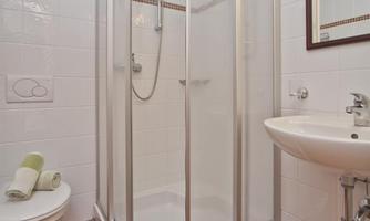 A modern bathroom with a shower cabin and a sink. The floor is tiled and the walls are light tiled.
