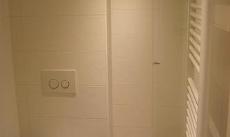 A modern bathroom with a shower and a toilet. The walls are kept in bright white, and there is underfloor heating.