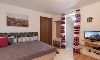 A cozy bedroom with a large bed and a television. The room has a bright atmosphere and decorative curtains.