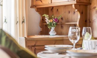 A cozy table with dishes and glasses, surrounded by warm wood paneling. On the sideboard stands a small vase with colorful flowers.