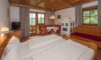 A cozy room with a double bed, wooden furniture, and large windows. There is a seating area with a table and a TV.