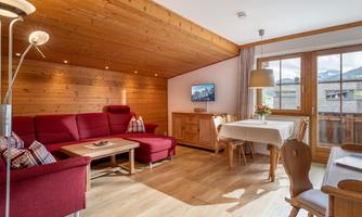 A cozy living room with red sofas and wooden walls. A dining table and large windows with a view outside complete the space.