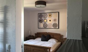 A cozy bedroom with a wooden bed and modern wall decor. The room has plenty of daylight and a calm atmosphere.