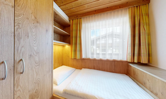 A cozy bedroom with wooden shelves and a large window. The curtains are bright and bring light into the room.