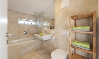 A modern bathroom with a bathtub and a sink. Light brown tiles and a wooden shelf with towels create a pleasant atmosphere.