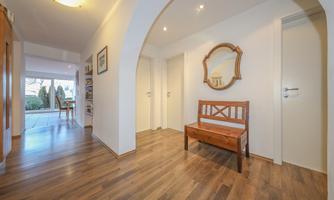 A bright hallway with wooden flooring and a wooden bench. A round mirror is hanging on the wall and there are doors to other rooms.