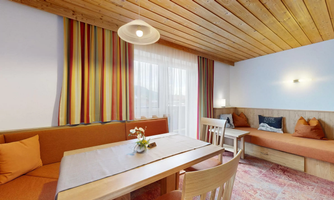 A cozy living space with wooden ceilings and colorful curtains. A large table and comfortable seating invite you to relax.