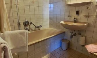 A simple bathroom with a bathtub and a sink. The walls are tiled, and there is a mirror above the sink.