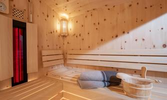 A cozy wooden sauna with benches and indirect lighting. A towel and a wooden ladle are ready.