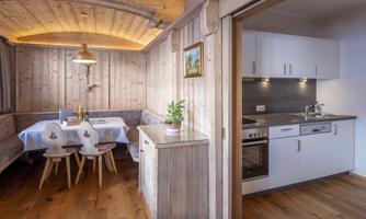 A bright and cozy kitchen with a wooden dining table and chairs. The walls are paneled with wood, and there is modern kitchen equipment.