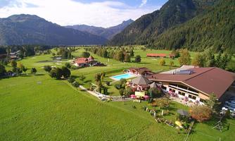 A picturesque landscape with a hotel and a swimming pool surrounded by green meadows and mountains. The backdrop conveys a sense of tranquility and relaxation.