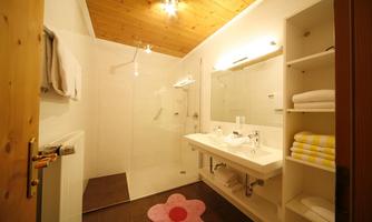 A modern bathroom with a shower and a bright, functional design. On the floor, there is a pink rug in the shape of a flower.