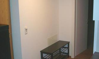 A simple hallway with a shoe rack and a wall coat rack. The floor is made of wood and the walls are painted light.