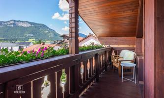 A beautiful wooden balcony with a view of the mountains. Blooming plants and a relaxed seating area complete the view.