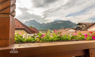 A beautiful view of the mountains with clouds in the sky. Colorful flowers adorn the balcony in the foreground.