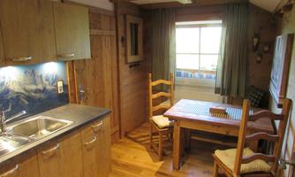 A cozy kitchen with wooden furniture and a dining table. The window offers a view of nature.