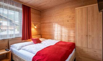 A cozy bedroom with wood paneling and a large bed.  
Red curtains and a warm atmosphere invite you to relax.