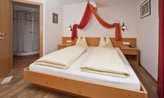 A cozy bedroom with a double bed and wooden details. The room is brightly designed and has a nice view of the bathroom.